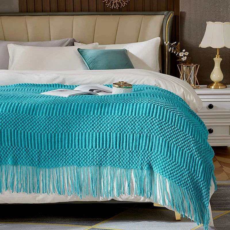 Knitted throw blanket with turquoise color and tassels on bed.