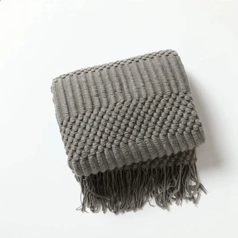 Knitted soft throw blanket with tassels in dark grey, featuring textured woven pattern.