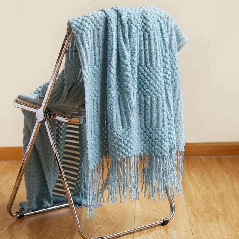 Knitted soft throw blanket with tassels in turquoise, draped over chair, showcasing texture and intricate patterns. Available in 10 colors.