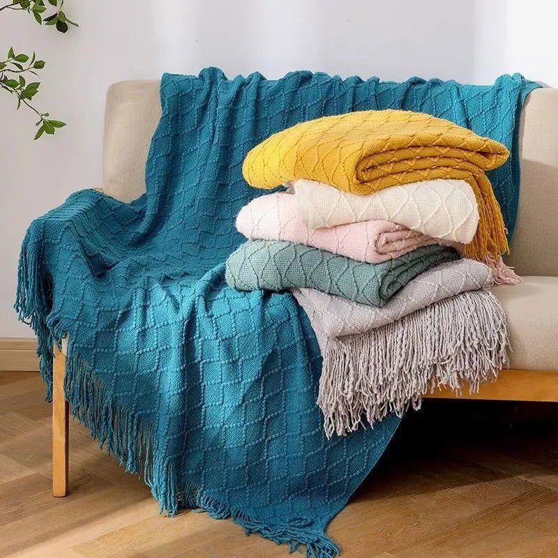 Knitted throw blanket with plaid pattern and tassels in multiple colors on a sofa.